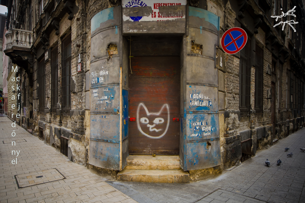 (DE) Ein altes, heruntergekommenes Gebäude mit geschlossenem Tor und einem Katzen-Graffiti in einer Straßenecke. (EN) A worn-down building with a closed gate and a cat graffiti in a street corner.