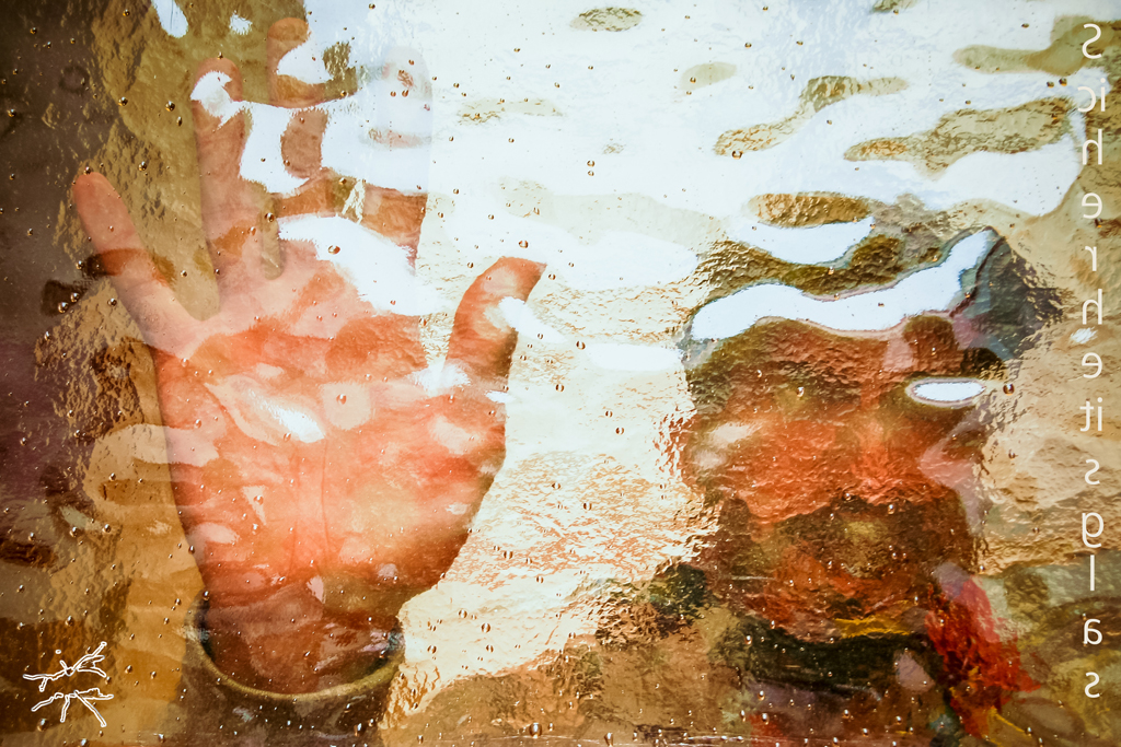 Deutsch: Eine Hand mit gespreizten Fingern drückt sich gegen strukturiertes Glas. Licht bricht sich an den Wellen, verzerrt die Konturen. Dahinter ein Gesicht, unscharf, entfernt, aber spürbar. Eine unsichtbare Grenze zwischen Nähe und Distanz. English: A hand with splayed fingers presses against textured glass. Light refracts through the ripples, distorting its form. Behind it, a blurred face—distant, yet present. An invisible boundary between closeness and distance.