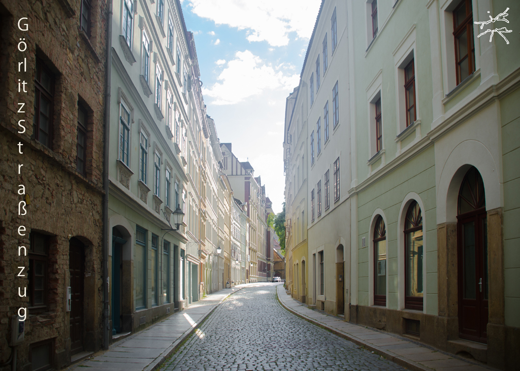 Ein leerer, gepflasterter Straßenzug in der Altstadt von Görlitz mit historischen Fassaden links und rechts bei Tageslicht.