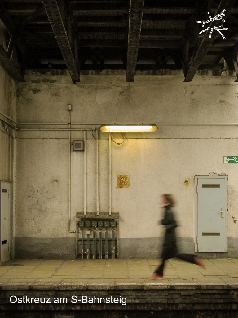 Deutsch:
Eine Frau eilt dem Ausgang entgegen, ihre Bewegung verwischt. Die Bahnsteighalle bleibt starr—abgenutzte Wände, rostiges Metall, gezeichnet von der Zeit. Ihr Tempo bricht die Stille, während das Gebäude bleibt, unbeeindruckt von den Schritten, die es durchqueren.
English:
A woman rushes toward the exit, her movement blurred. The station remains still—worn walls, rusted metal, marked by time. Her speed cuts through the silence, while the structure endures, unmoved by the footsteps that pass through it.