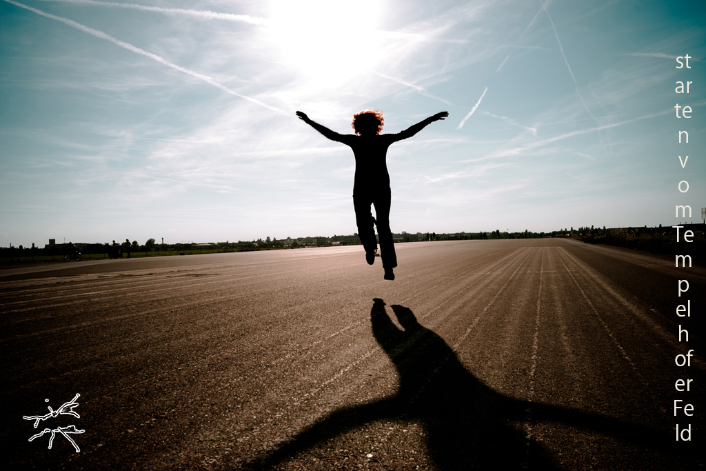 Silhouette einer springenden Person auf der Landebahn des Tempelhofer Felds in Berlin, mit ausgebreiteten Armen vor hellem Himmel.