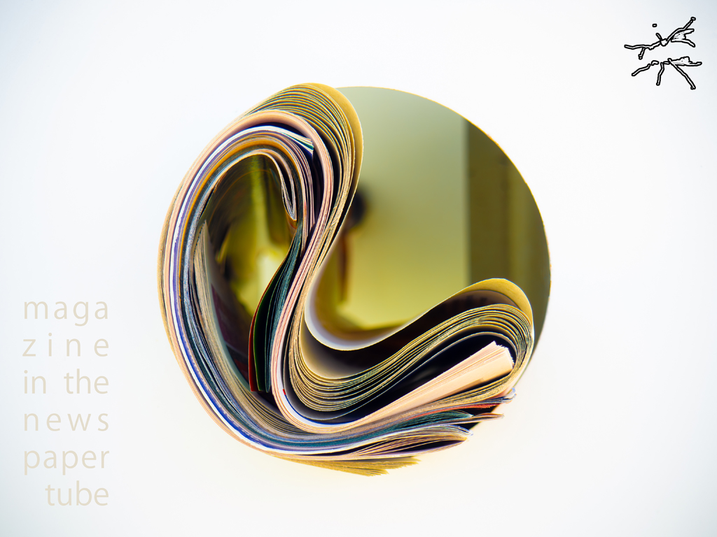 Ein eingerolltes Magazin in einer goldenen Röhrenform, von oben fotografiert – das Papier wirkt wie eine skulpturale Welle aus Farbe und Struktur, eingefroren im Licht.