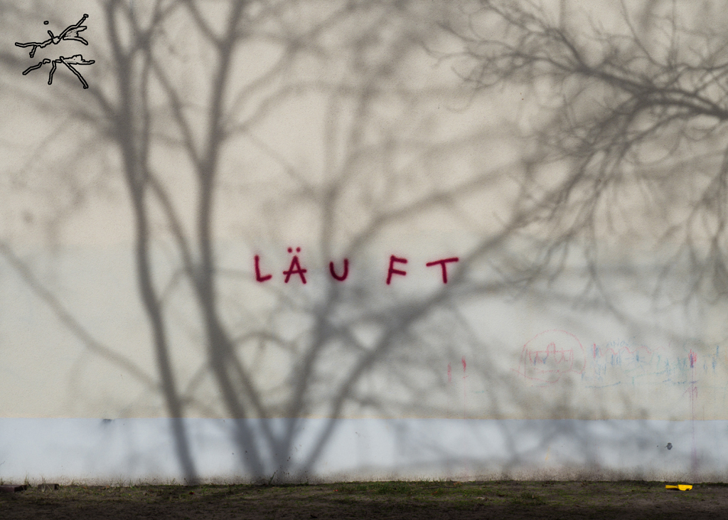 Graffiti „LÄUFT“ in Rot auf beiger Wand mit Schatten von kahlen Ästen – still, doch in Bewegung.