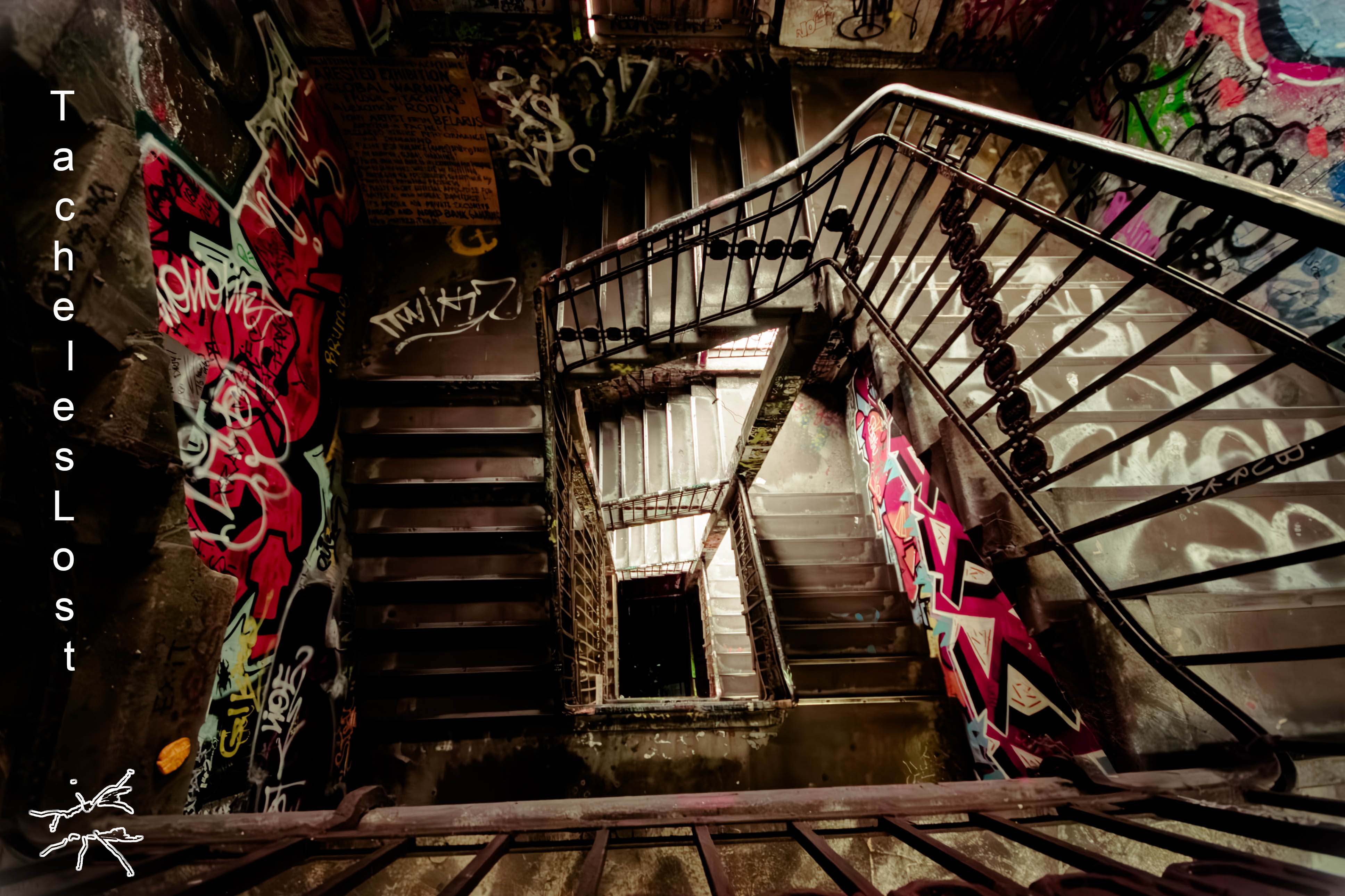 Deutsch: Ein Berliner Treppenhaus windet sich abwärts, die Wände überzogen mit verblasstem Graffiti aus der Vergangenheit des Tacheles. Spuren von Kunst, Geschichte und Vergänglichkeit. English: A Berlin stairwell spirals downward, its walls covered in faded graffiti from Tacheles’ past. Traces of art, history, and transience linger.