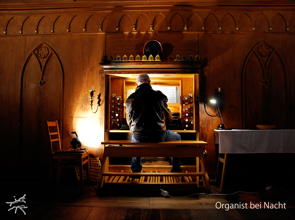 Deutsch: In schwachem Licht bewegt der Organist seine Hände mit ruhiger Präzision über die Tasten. Das dunkle Holz schimmert, als würde es den Klang tragen. Schatten tanzen in den Kirchenbögen, während die Musik den Raum erfüllt – ein stiller Dialog zwischen Mensch und Instrument. English: In dim light, the organist moves his hands with quiet precision across the keys. The dark wood gleams as if carrying the sound. Shadows dance in the church’s arches as the music fills the space—a silent dialogue between man and instrument.
