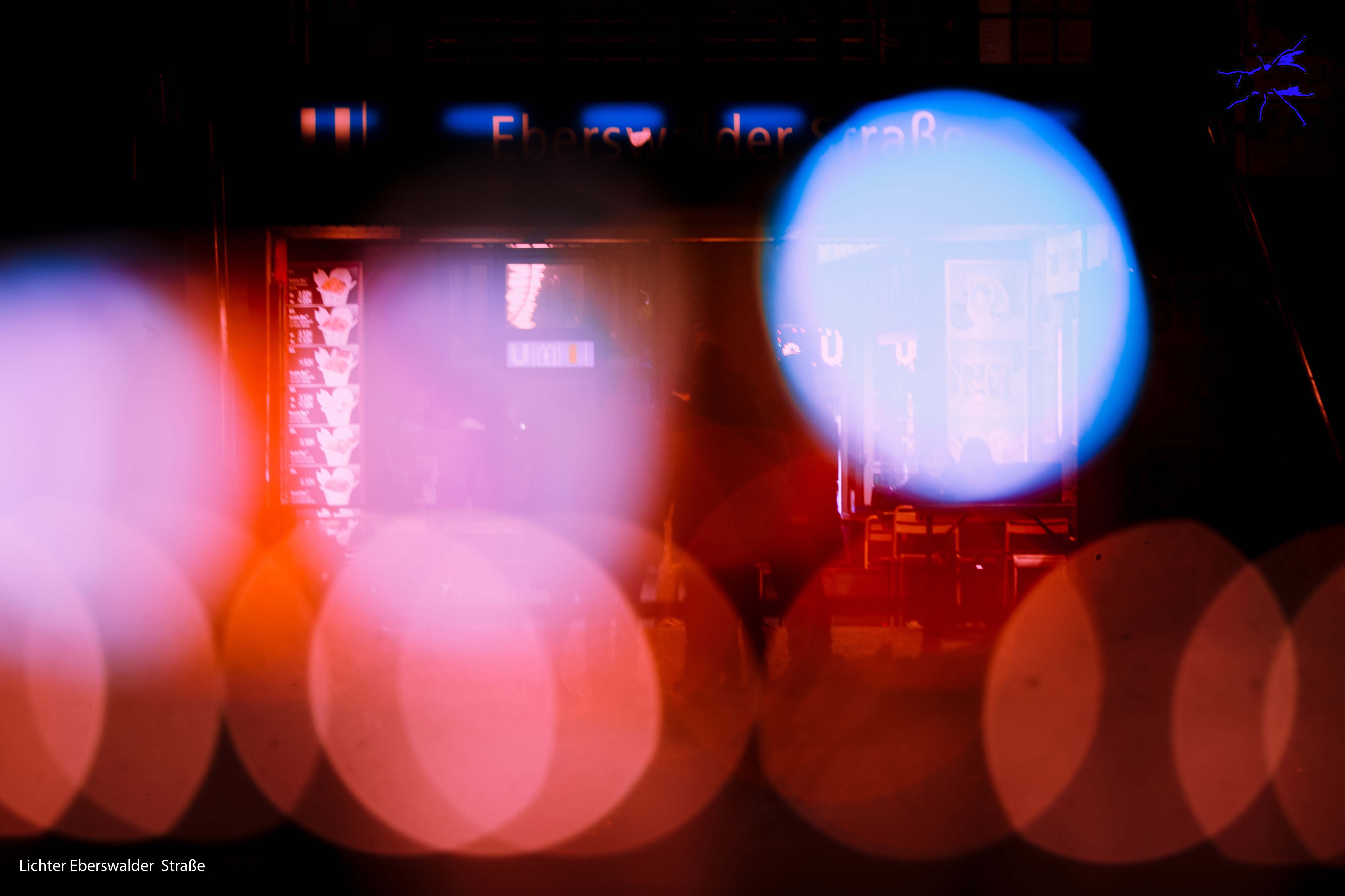 Deutsch: Ein urbaner nächtlicher Blick auf Berlin, durchzogen von Lichtreflexen und verschwommenen Farbmustern. Eine Szenerie aus Glas, Beton und Bewegung, in der sich Reflexionen mit der Lebendigkeit der Stadt verweben. English: An urban night scene of Berlin, streaked with light reflections and blurred color patterns. A setting of glass, concrete, and movement, where reflections blend with the city’s vibrancy.