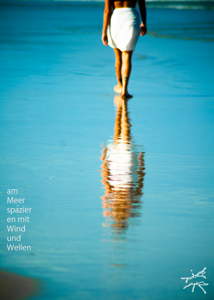 Person in weißem Tuch beim Spaziergang am Meer, mit Spiegelung im nassen Sand