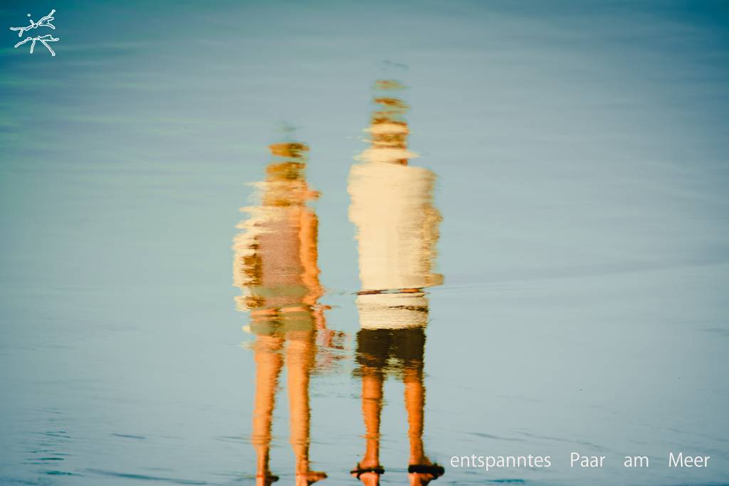 Spiegelung eines Paares im seichten Wasser am Strand, unscharf und atmosphärisch