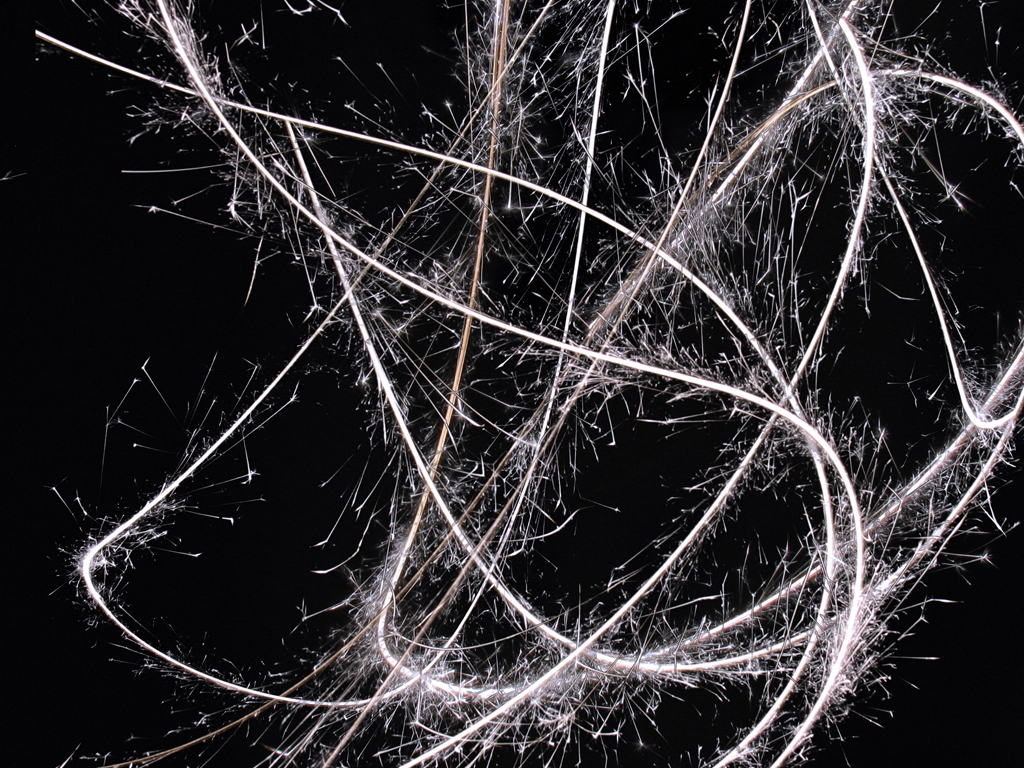 Abstrakte Langzeitbelichtungsfotografie: Weiße, chaotische Lichtspuren kreuzen sich dynamisch auf schwarzem Hintergrund. Abstract long-exposure photography: White, chaotic light trails cross dynamically on a black background.