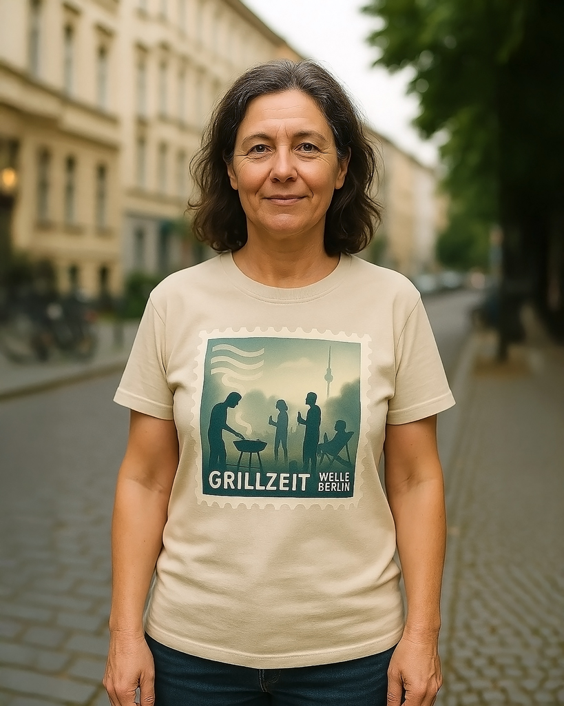(DE) Frau steht in einer Berliner Straße und trägt ein T-Shirt mit dem Motiv „Grillzeit – Welle Berlin“, das Menschen beim Grillen als grafische Szene zeigt. (EN) A woman standing on a Berlin street wearing a T-shirt featuring the design “Grillzeit – Welle Berlin,” showing a graphic scene of people grilling.