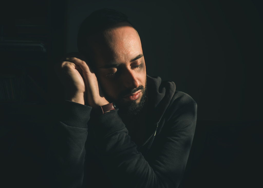 Portraitfotografie als Wahrnehmung. Portrait eines Mannes mit geschlossenen Augen im warmen Seitenlicht vor dunklem Hintergrund