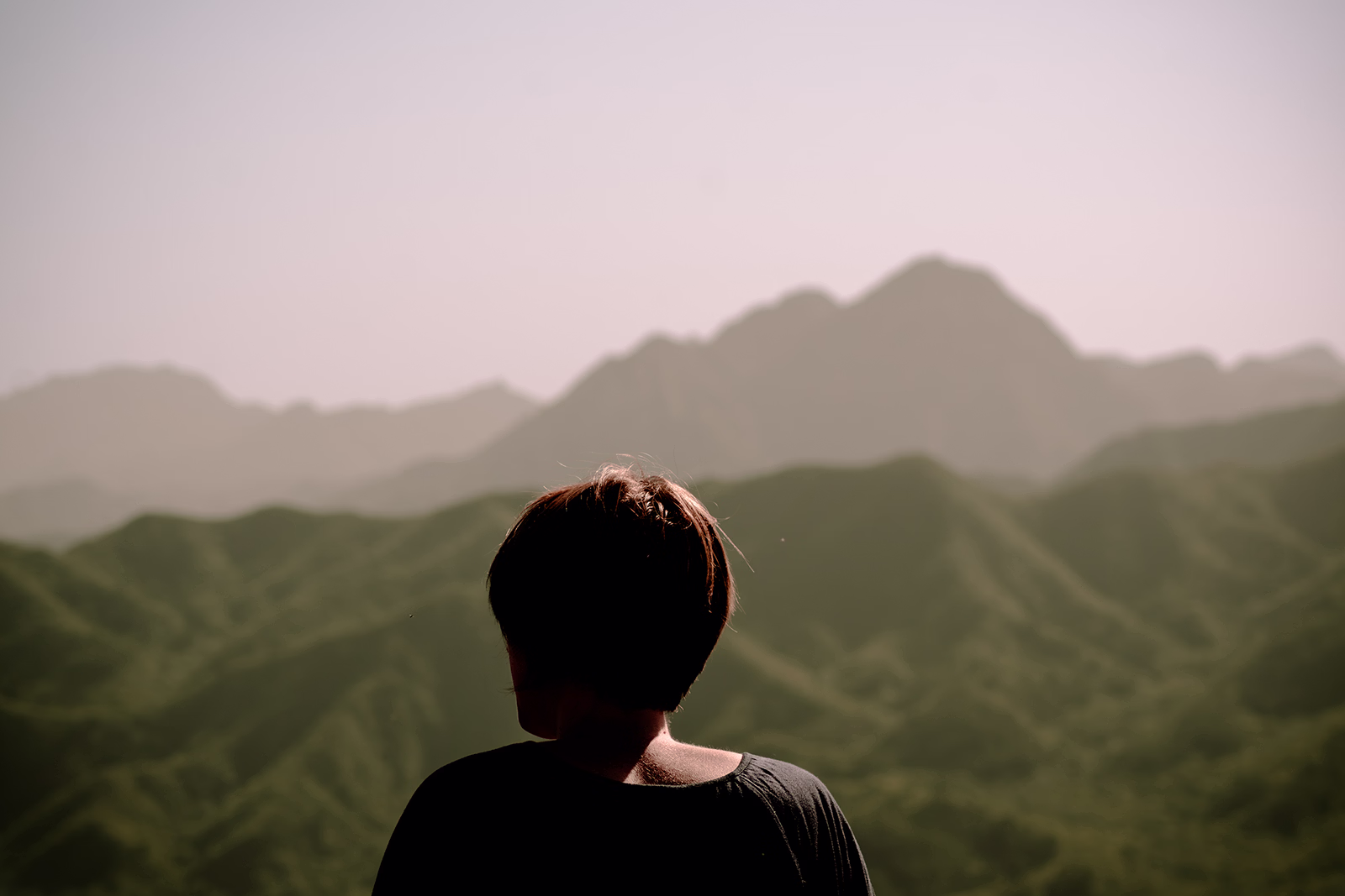 Fotograf in Berlin – Portraits und Serien – Begegnungen in Bildern. Eine Person steht mit dem Rücken zur Kamera, blickt über eine weite, grüne Hügellandschaft. Das Licht ist weich, die Atmosphäre ruhig – als wäre dies ein Moment des Innehaltens. Der Text überlagert das Bild, spricht von Begegnungen, ungesagten Worten und flüchtigen Augenblicken, die in ihrer Echtheit bleiben.